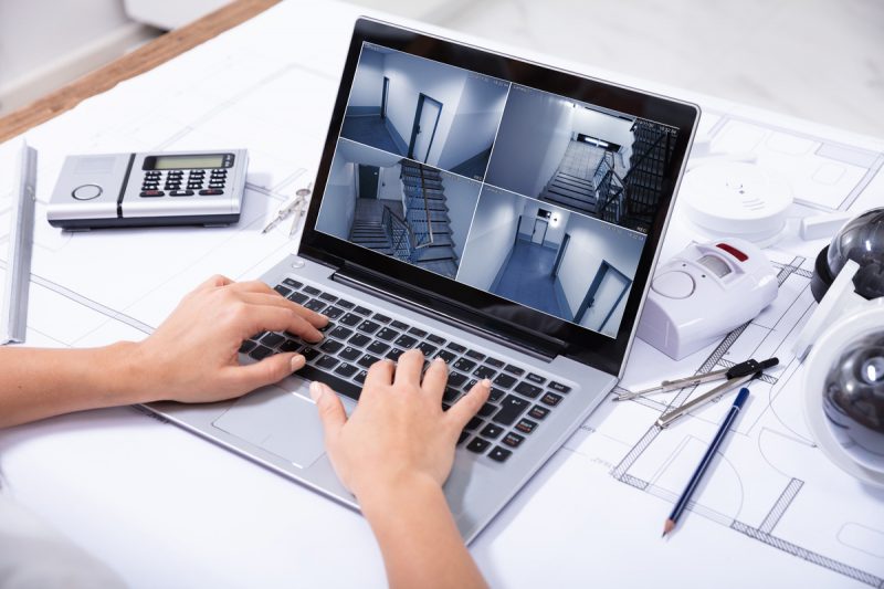 Close-up Of A Woman Monitoring Home Security Cameras On Laptop Over The Blue Print