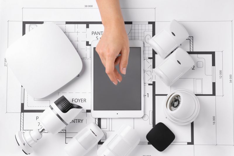 Female hand with tablet computer and different equipment of security system on home plan